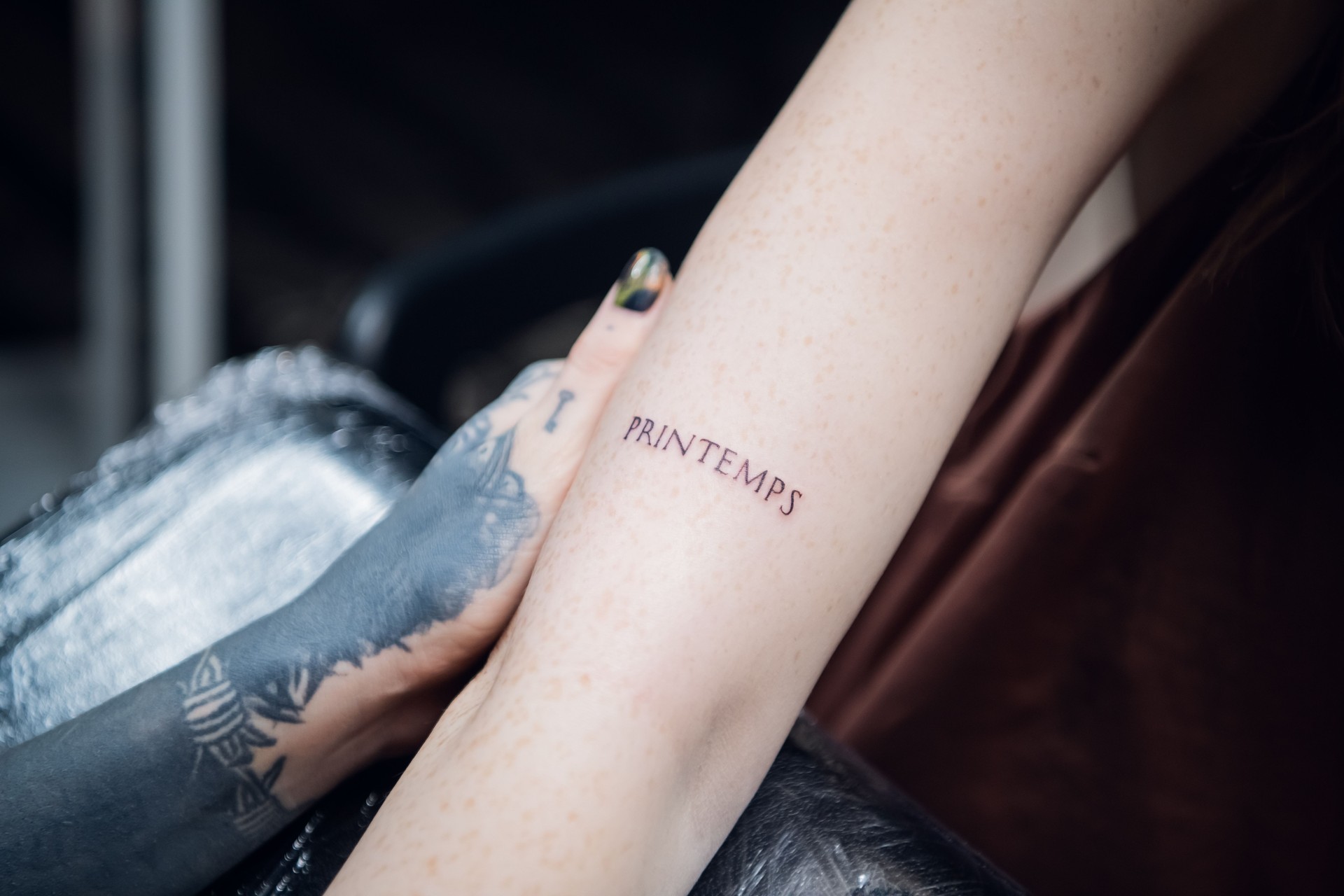 The hand of a tattoo artist a girl with tattoos and a newly made tattoo in the form of a word on the hand of a freckled client